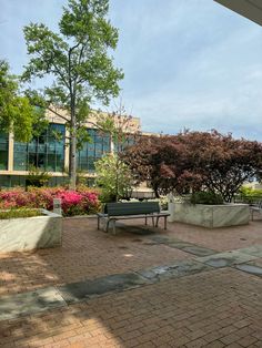 a park bench sitting on top of a brick walkway next to trees and flowers in front of a building