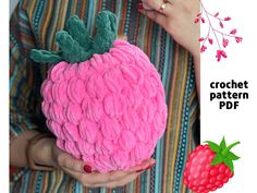 a woman holding a crochet pattern for a strawberry pillow with green leaves on it