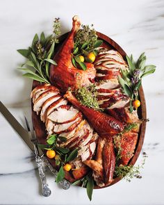 a roasted turkey on a platter with sage and lemons, surrounded by greenery