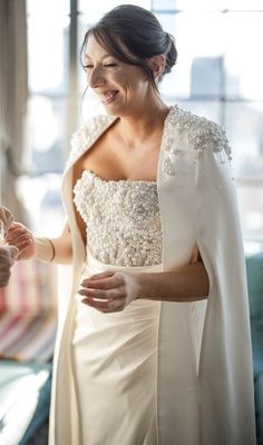 a woman in a white dress is smiling and holding her hand out to another person