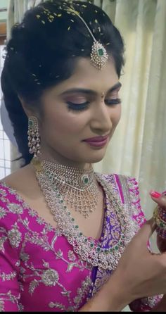 a woman in a pink sari is looking at her cell phone while wearing jewelry