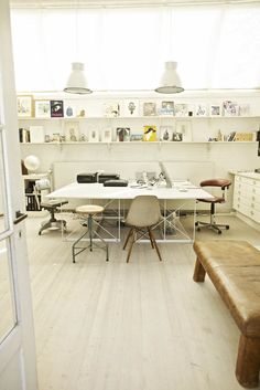 a room with white walls and wooden floors has a long table, two chairs, an office bench, and several bookshelves