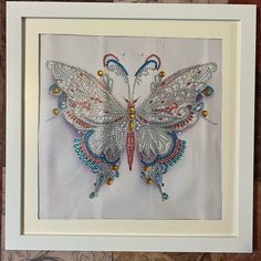 an embroidered butterfly is displayed in a white frame