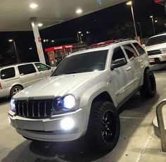 a white jeep is parked in front of a gas station at night with its lights on