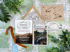 the wedding stationery is laid out on top of a map and some greenery