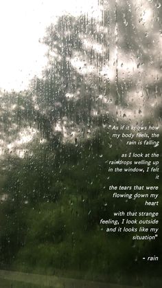 rain is falling down on the window with a poem written in it and trees outside