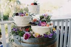 three tiered wedding cake on top of a barrel with purple flowers and greenery