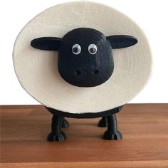 a black sheep wearing a white hat on top of a wooden table next to a wall