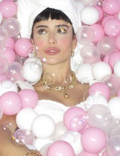 a woman in a bathtub surrounded by pink and white balls, with her eyes closed