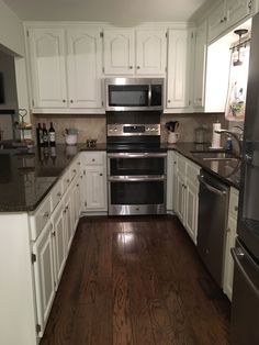 an empty kitchen with white cabinets and stainless steel appliances, wood flooring and granite counter tops