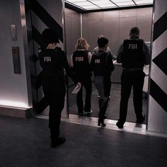 four people in black uniforms are standing at an elevator door with their backs to the camera