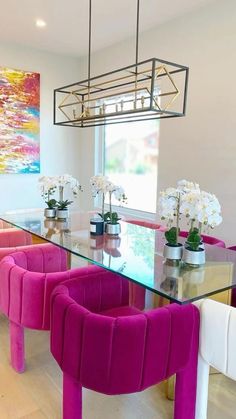 a dining room table with pink chairs and white flowers in vases on the glass top