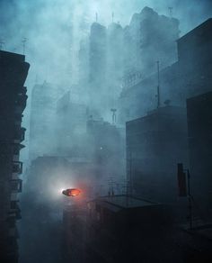 a car driving down a foggy city street in the middle of the night with tall buildings