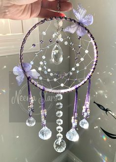 a hand is holding a purple and white dream catcher with butterflies on the side,