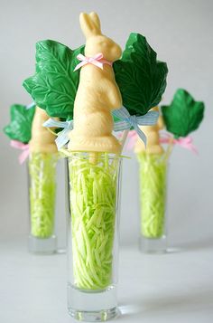 three small glass vases filled with green grass and plastic bunny figurines sitting on top of each other