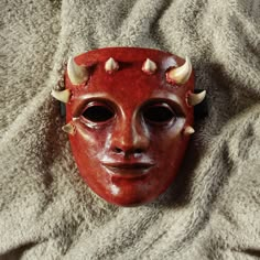 a red mask with horns and spikes on it's head laying on a blanket