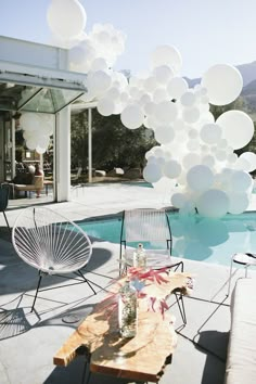 balloons are floating in the air over a table and chairs near a swimming pool with mountains in the background