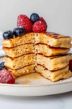 stack of pancakes topped with berries and powdered sugar on a white plate, ready to be eaten