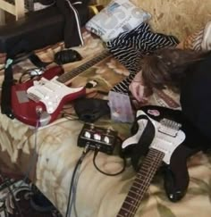 a woman laying on top of a bed next to two electric guitars and an amp