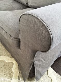 a gray couch sitting on top of a wooden floor next to a rug and pillow