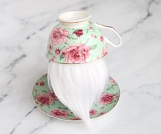 a green and pink flowered tea cup with a white beard on the saucer