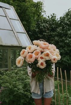 a woman holding a bunch of flowers in front of a greenhouse with lots of plants