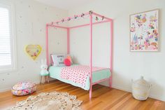 a pink canopy bed sitting on top of a hard wood floor next to a white wall