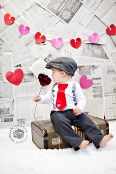 a little boy sitting on top of a suitcase in the snow wearing a tie and holding a flower