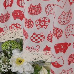 a red and white curtain with cats on it is next to flowers in a vase