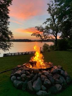 a fire pit sitting on top of a lush green field next to a body of water