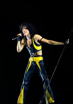 the man is dressed in black and yellow with his arms out, holding a microphone