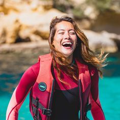 a woman wearing a red life jacket smiles while standing in the water with her mouth open