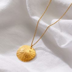 The Gold Plated Large Sand Dollar Necklace is a beautifully crafted piece of jewellery, capturing the delicate and intricate design of a sand dollar in precious metal. The pendant itself i an organic circular disc, textured to resemble the natural patterns found on a real sand dollar, with subtle details that highlight its elegance.   The necklace is made from Sterling Silver plated in a warm 18ct yellow gold, suspended from a fine chain that complements the pendant's minimalist yet sophisticated appearance.  Whether worn alone or layered with other pieces, the Large Sand Dollar Necklace is a versatile and striking addition to your jewellery collection making it a perfect accessory for those who appreciate both nature and refined elegance. 925 Sterling Silver with 18ct yellow gold plating. Aesthetic Essentials, Sand Dollar Necklace, Posh Totty, Dubai Gold Jewelry, Cowrie Shell Necklace, Natural Patterns, Cowrie Shell, Sand Dollar, Timeless Jewelry