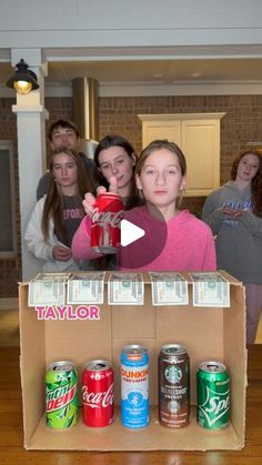 a group of young women standing around a box with cans in it and one woman pointing at the camera