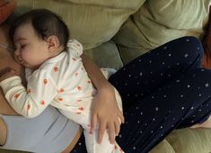 a woman laying on top of a couch holding a baby