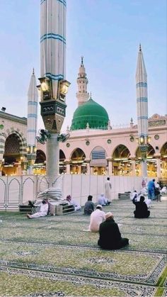 people sitting on the ground in front of a building with green domes and minas