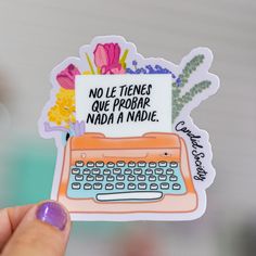 a person holding up a sticker with an old typewriter on it and flowers in the background