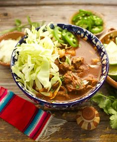 a bowl filled with meat and veggies on top of a wooden table next to other foods