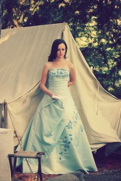 a woman in a blue dress standing next to a tent