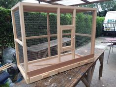 a large bird cage sitting on top of a wooden table next to a green bush