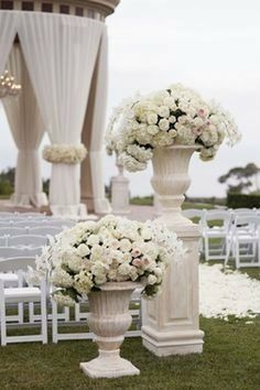 two white urns with flowers on them sitting in the grass at a wedding ceremony