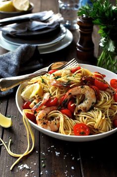 a white bowl filled with pasta and shrimp next to lemon wedges on a wooden table