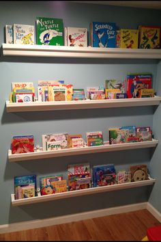 two white shelves filled with books on top of a blue wall next to a wooden floor