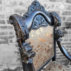 an ornately decorated chair sitting in front of a brick wall with peeling paint on it