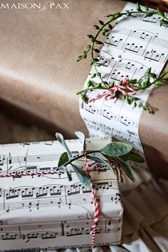 sheet music wrapping paper with holly and red striped twine tied to it, sitting on top of a pile of christmas presents