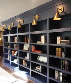 the bookshelves are lined up against the wall with gold lamps on each side