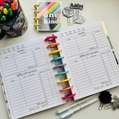 an open planner with pens and markers on it next to a cup of crayons