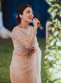 a woman in a white sari singing into a microphone