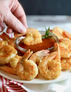 a person dipping sauce on shrimp on a white plate with red and white striped napkin