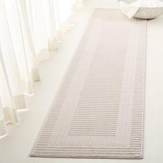 a white rug on the floor in front of a window with curtains and a bowl